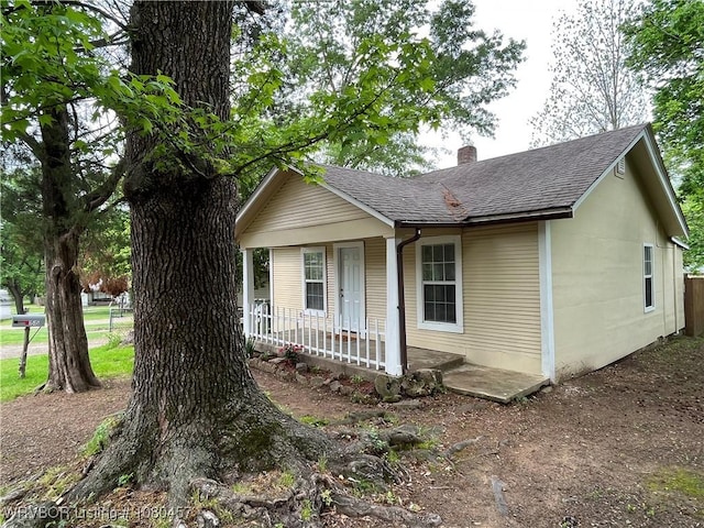 view of front of house featuring a porch, a shingled roof, and a chimney