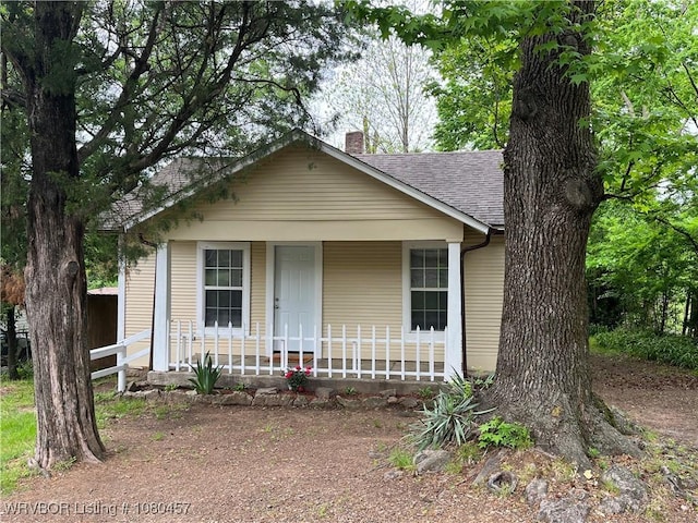 bungalow with a porch, roof with shingles, fence, and a chimney