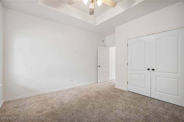 unfurnished bedroom featuring baseboards, a raised ceiling, crown molding, carpet flooring, and a closet