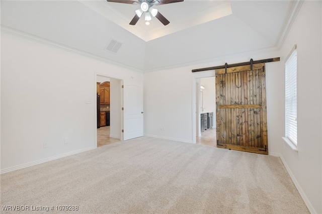 unfurnished bedroom featuring carpet floors, a tray ceiling, visible vents, a barn door, and ornamental molding