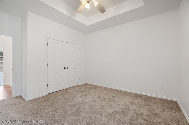 unfurnished bedroom featuring baseboards, a closet, a tray ceiling, carpet, and crown molding