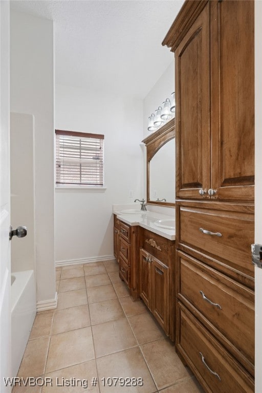 bathroom featuring baseboards, double vanity, a sink, and tile patterned floors