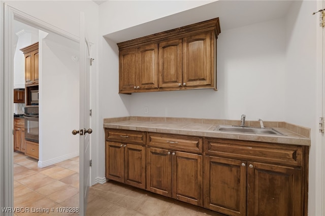 kitchen featuring black microwave, a sink, tile counters, range, and brown cabinetry