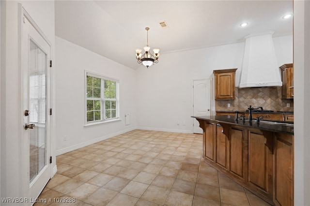 kitchen featuring dark countertops, custom range hood, a breakfast bar area, a chandelier, and backsplash