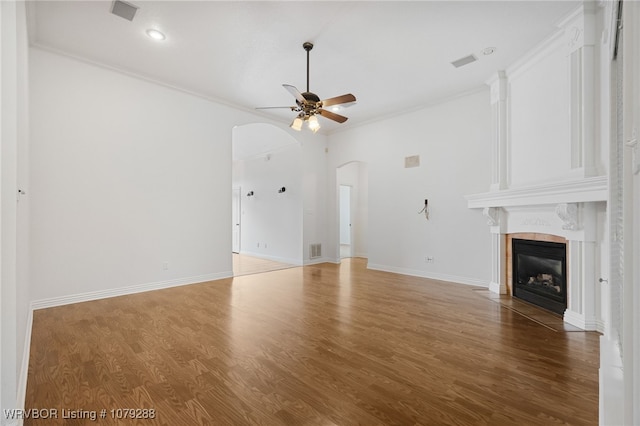 unfurnished living room with arched walkways, a fireplace, visible vents, ceiling fan, and wood finished floors