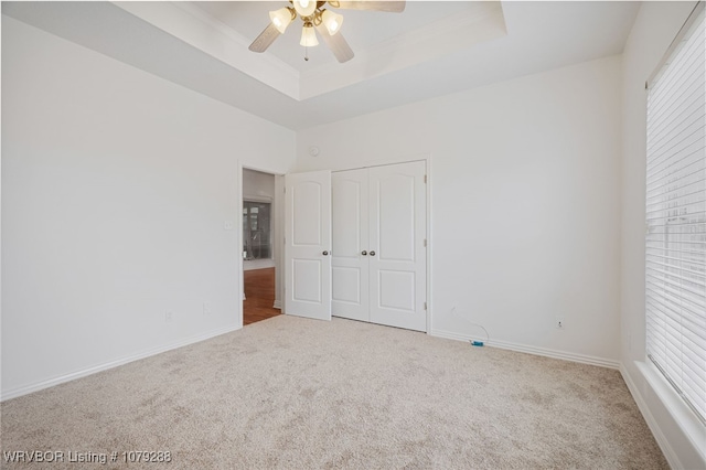 unfurnished bedroom with baseboards, a raised ceiling, ceiling fan, carpet, and a closet