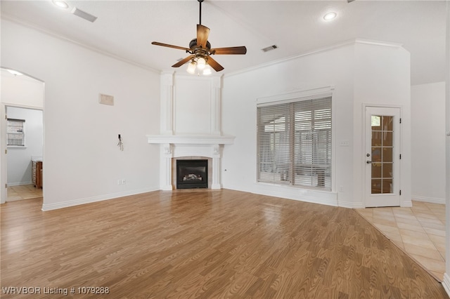 unfurnished living room with a large fireplace, arched walkways, light wood finished floors, and crown molding