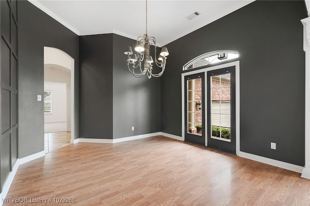 empty room featuring arched walkways, light wood-type flooring, visible vents, and baseboards