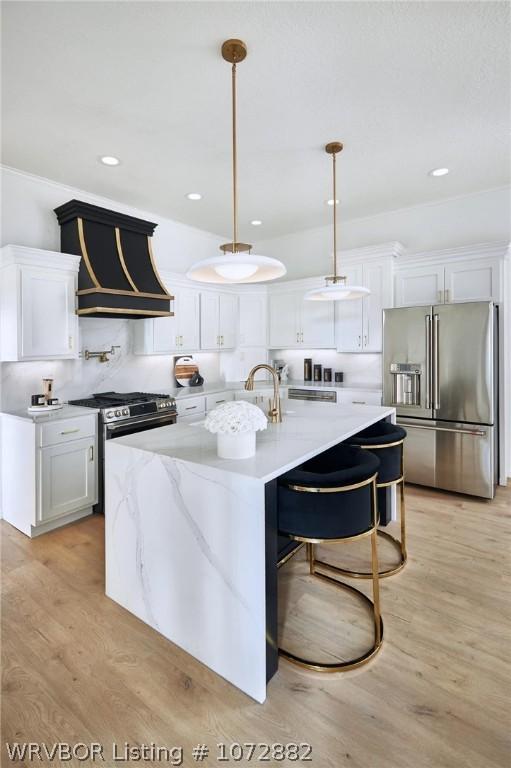 kitchen featuring appliances with stainless steel finishes, decorative light fixtures, white cabinets, light hardwood / wood-style floors, and an island with sink