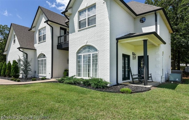 view of front of house featuring a balcony, central AC, and a front lawn