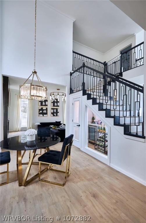 dining area featuring wood-type flooring, crown molding, a towering ceiling, and a chandelier