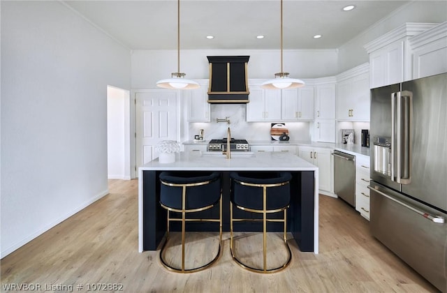 kitchen with white cabinetry, premium range hood, decorative light fixtures, a kitchen island with sink, and appliances with stainless steel finishes