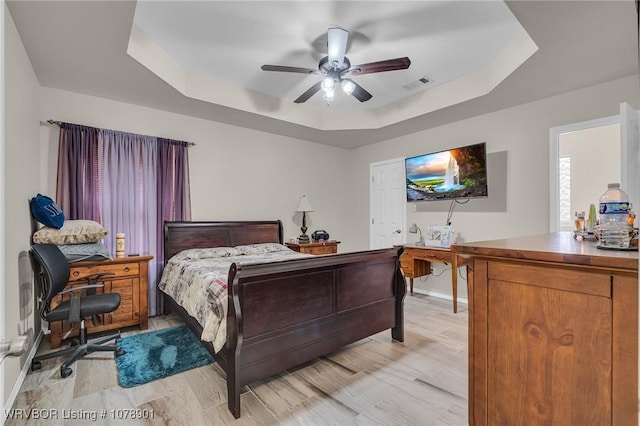 bedroom with ceiling fan, light wood-type flooring, and a tray ceiling