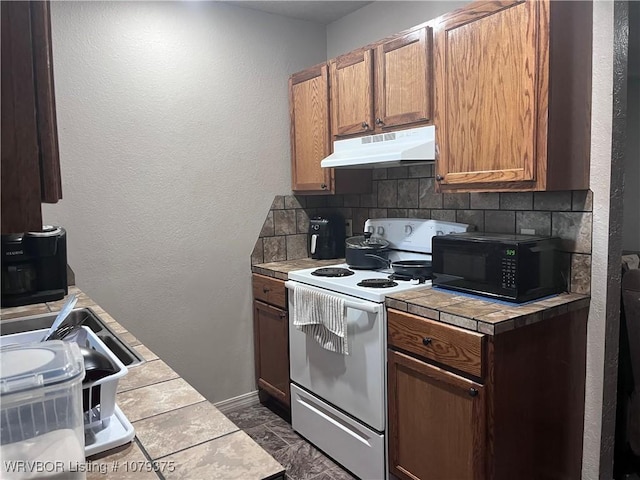 kitchen with tasteful backsplash, black microwave, tile counters, under cabinet range hood, and white range with electric stovetop