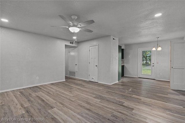 unfurnished living room featuring wood finished floors, a chandelier, a ceiling fan, a textured ceiling, and baseboards