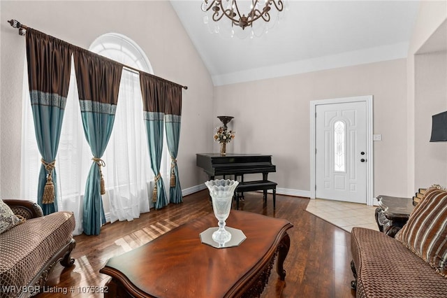 living room featuring lofted ceiling, baseboards, wood finished floors, and a notable chandelier