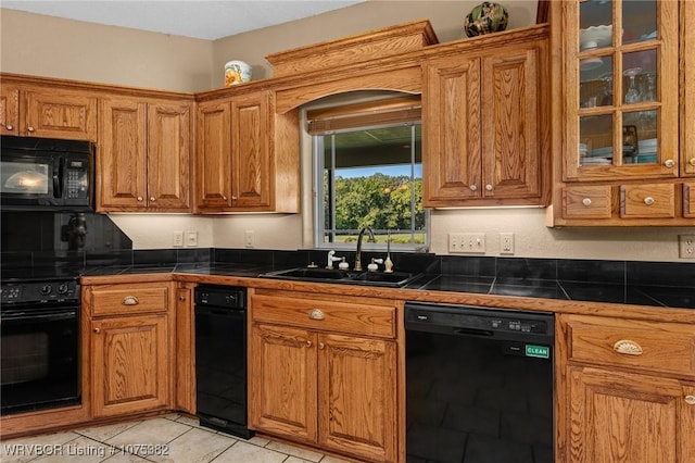 kitchen featuring dark countertops, brown cabinets, a sink, and black appliances