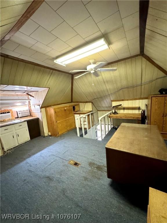 bonus room with ceiling fan, wood walls, dark carpet, and vaulted ceiling