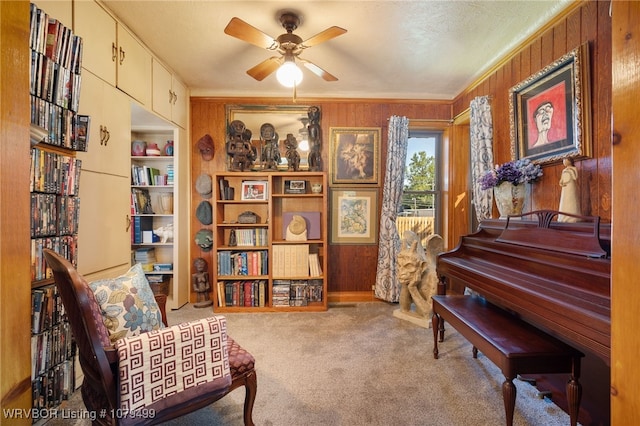 living area with carpet, ceiling fan, crown molding, and wood walls