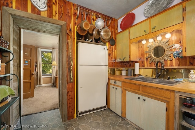 kitchen with wooden walls, freestanding refrigerator, a sink, light countertops, and dark carpet