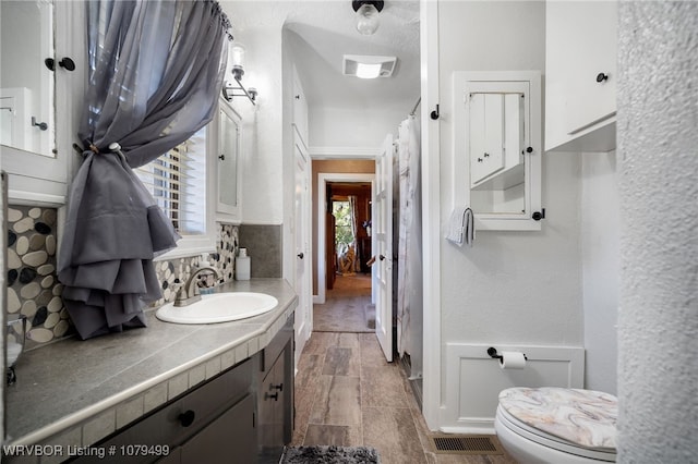 bathroom with visible vents, backsplash, vanity, and toilet