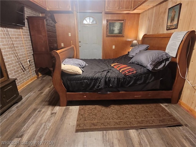 bedroom featuring hardwood / wood-style floors, wooden walls, and brick wall