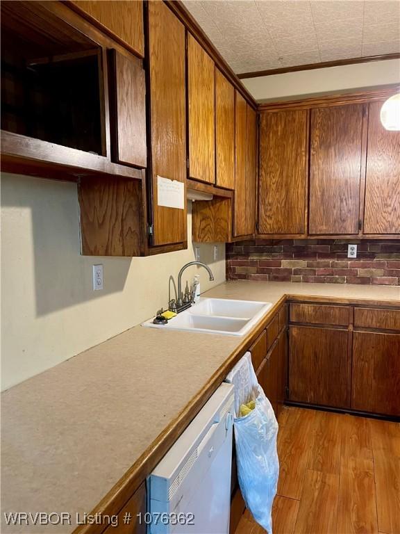 kitchen with dishwasher, crown molding, sink, decorative backsplash, and light wood-type flooring