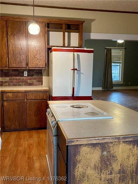 kitchen featuring white refrigerator, backsplash, range with electric stovetop, light hardwood / wood-style floors, and decorative light fixtures