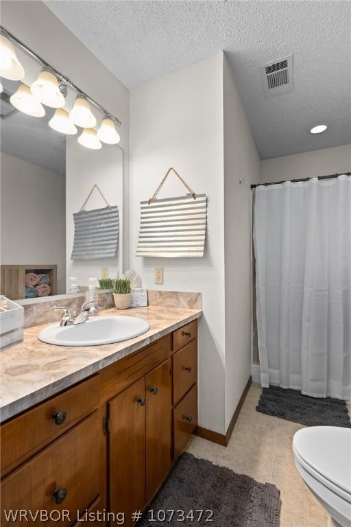 bathroom with tile patterned floors, vanity, a textured ceiling, and toilet