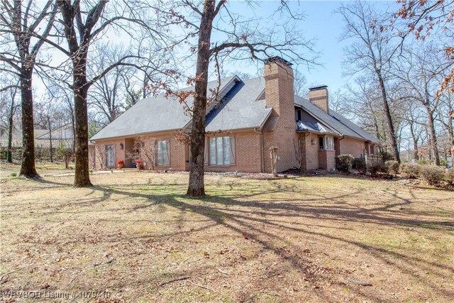 view of side of home with brick siding, a lawn, and a chimney