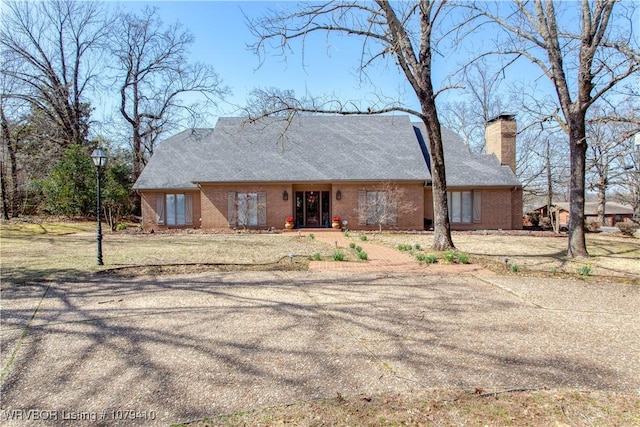 view of front of property featuring brick siding, a chimney, and a front lawn