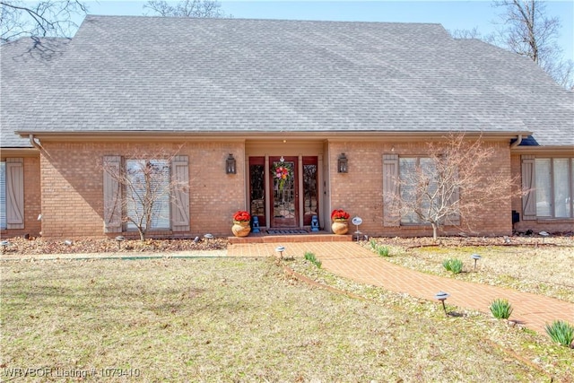 rear view of property featuring a yard, brick siding, and roof with shingles