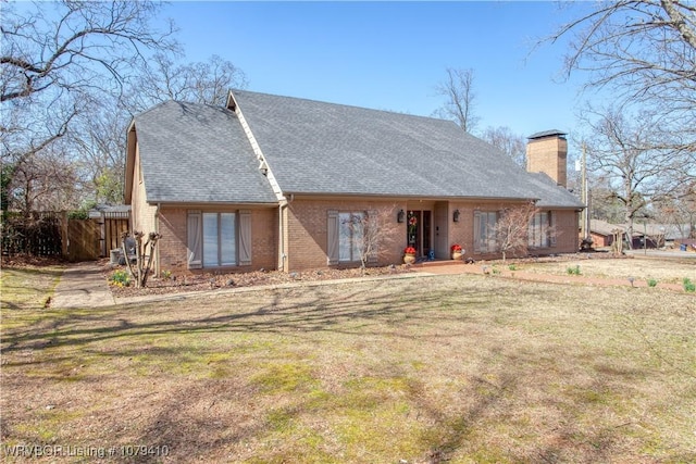 view of front of house with a front yard, brick siding, roof with shingles, and a chimney