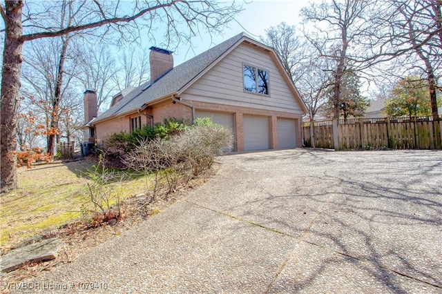 view of home's exterior with driveway, fence, an attached garage, brick siding, and a chimney