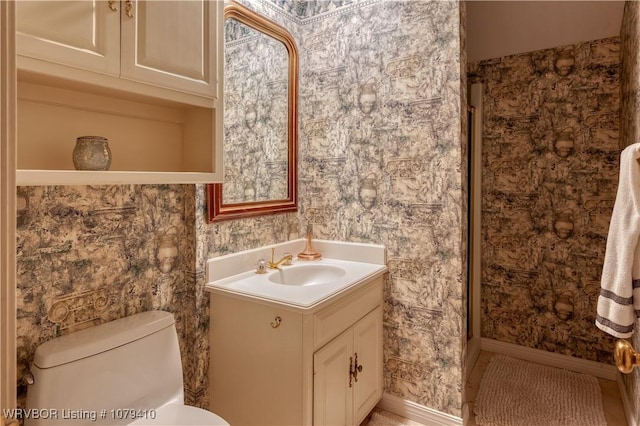 bathroom featuring toilet, wallpapered walls, baseboards, walk in shower, and vanity