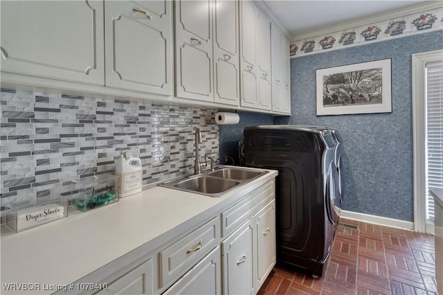 laundry area featuring a sink, cabinet space, wallpapered walls, brick floor, and baseboards