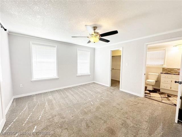 unfurnished bedroom featuring ensuite bath, ornamental molding, ceiling fan, a spacious closet, and a closet