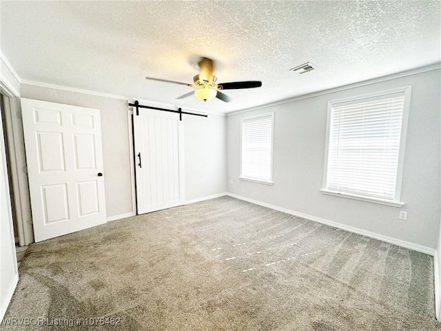 unfurnished room with ceiling fan, a barn door, carpet floors, a textured ceiling, and ornamental molding