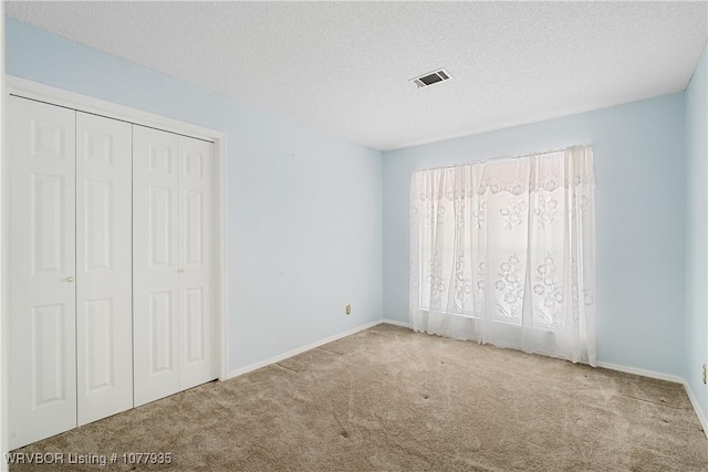 unfurnished bedroom with light carpet, a textured ceiling, multiple windows, and a closet