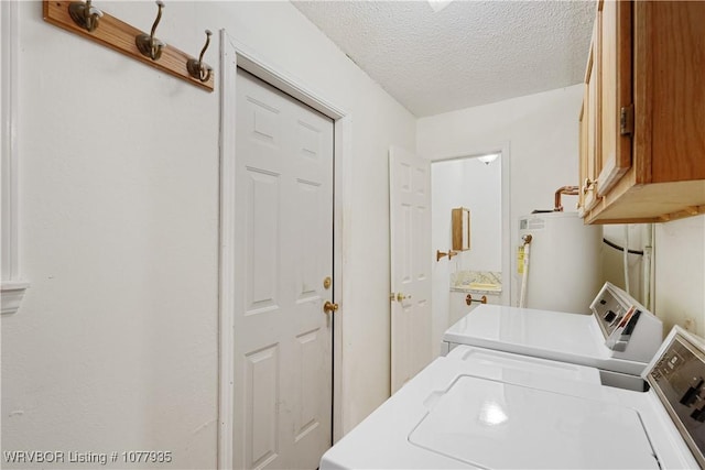 laundry room with washer and clothes dryer, cabinets, a textured ceiling, and water heater