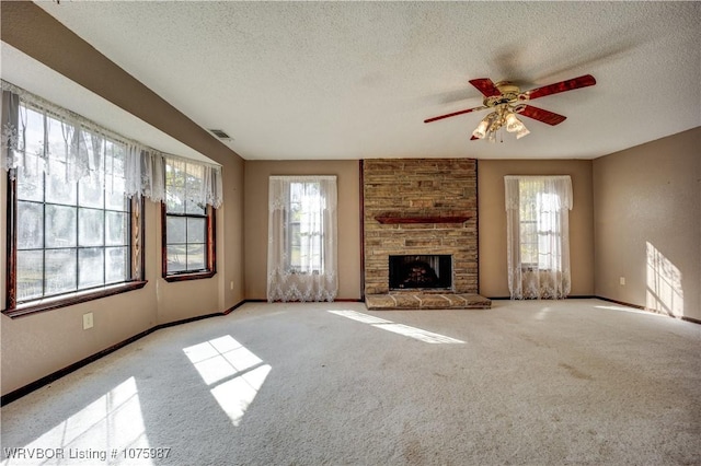 unfurnished living room with ceiling fan, a healthy amount of sunlight, a stone fireplace, light colored carpet, and a textured ceiling