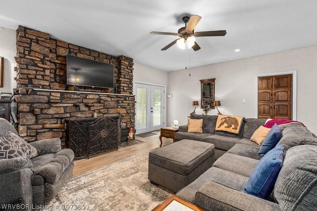 living room with a stone fireplace, ceiling fan, french doors, and light hardwood / wood-style floors