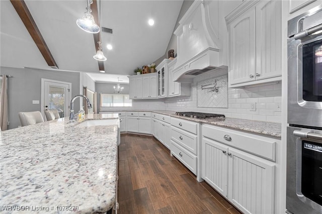 kitchen featuring decorative backsplash, custom range hood, appliances with stainless steel finishes, light stone counters, and white cabinetry