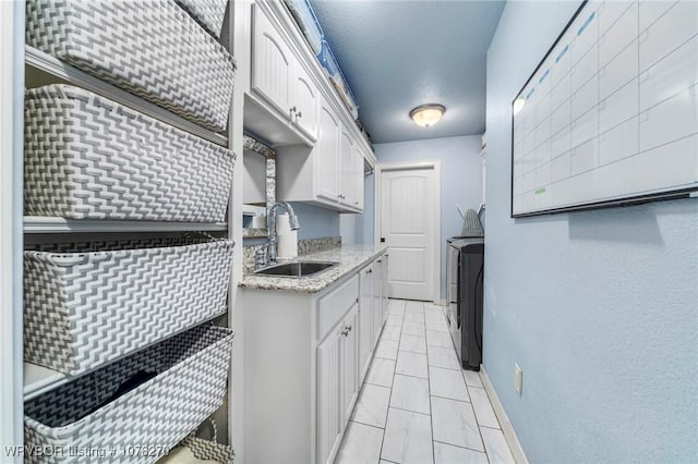 kitchen featuring light stone counters, a textured ceiling, sink, separate washer and dryer, and white cabinets