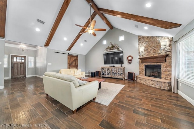 living room with ceiling fan with notable chandelier, a barn door, high vaulted ceiling, beamed ceiling, and a stone fireplace