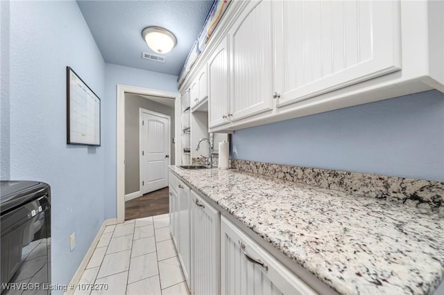 kitchen featuring light stone countertops, a textured ceiling, white cabinetry, and sink