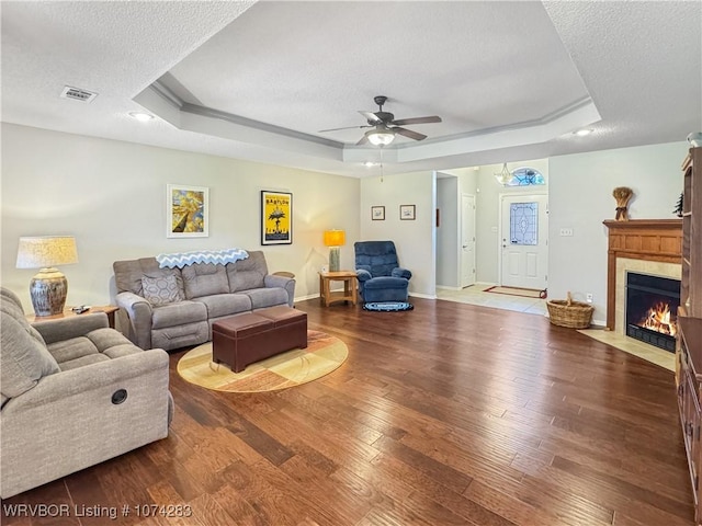 living room featuring a raised ceiling, ceiling fan, wood-type flooring, and a textured ceiling