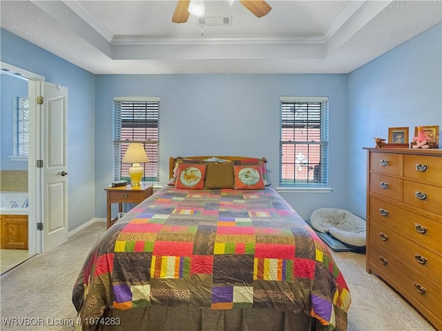 bedroom featuring light carpet, a tray ceiling, ensuite bath, and ceiling fan