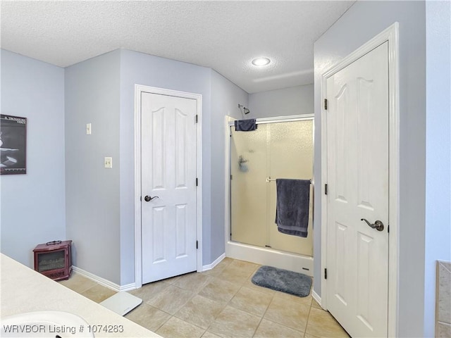 bathroom featuring tile patterned floors, a shower with door, vanity, and a textured ceiling