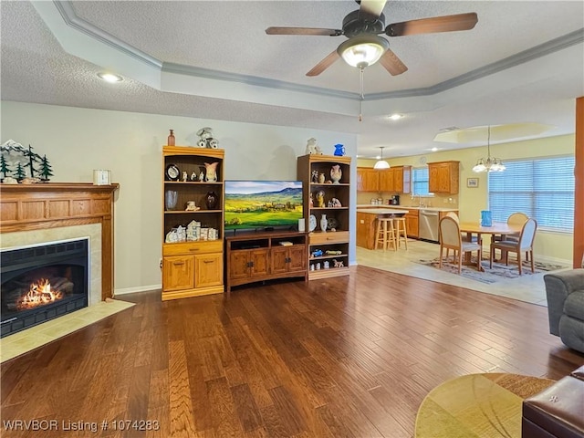 living room featuring ceiling fan with notable chandelier, a raised ceiling, crown molding, a fireplace, and dark hardwood / wood-style floors